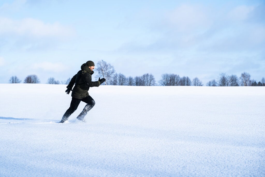 Photo of a male running on in the field covered in snow.