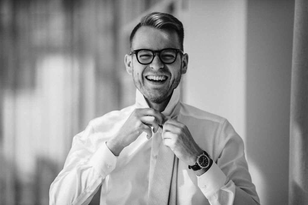 Black and white portrait photo of a young man smiling while doing his tie