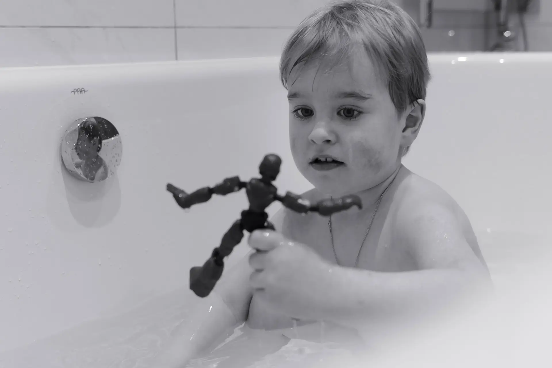 Young boy playing with an action figure during bath time, captured in a candid black and white photo.