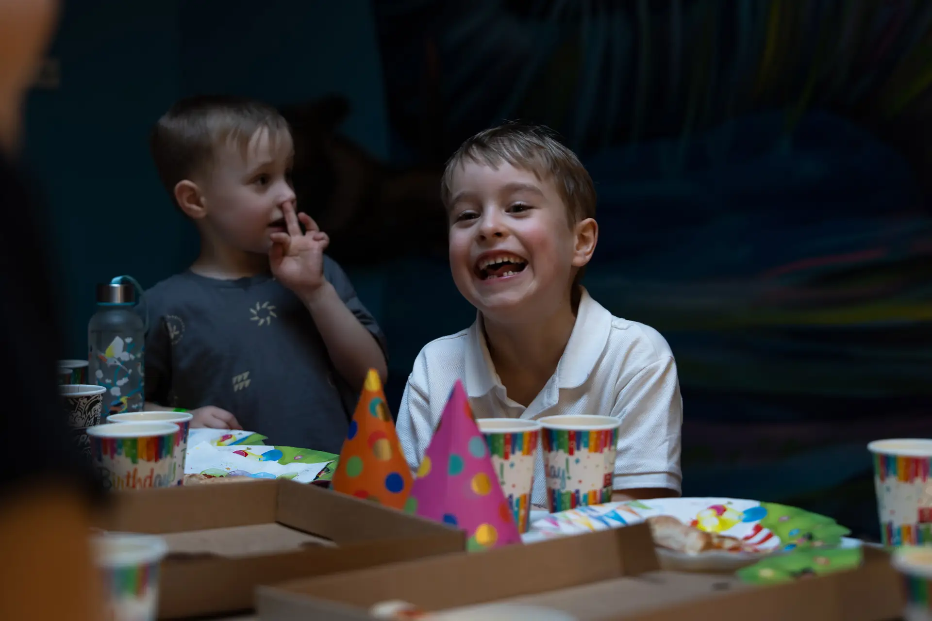 Smiling young boy celebrating at a birthday party with colorful hats, cups, and pizza on the table.