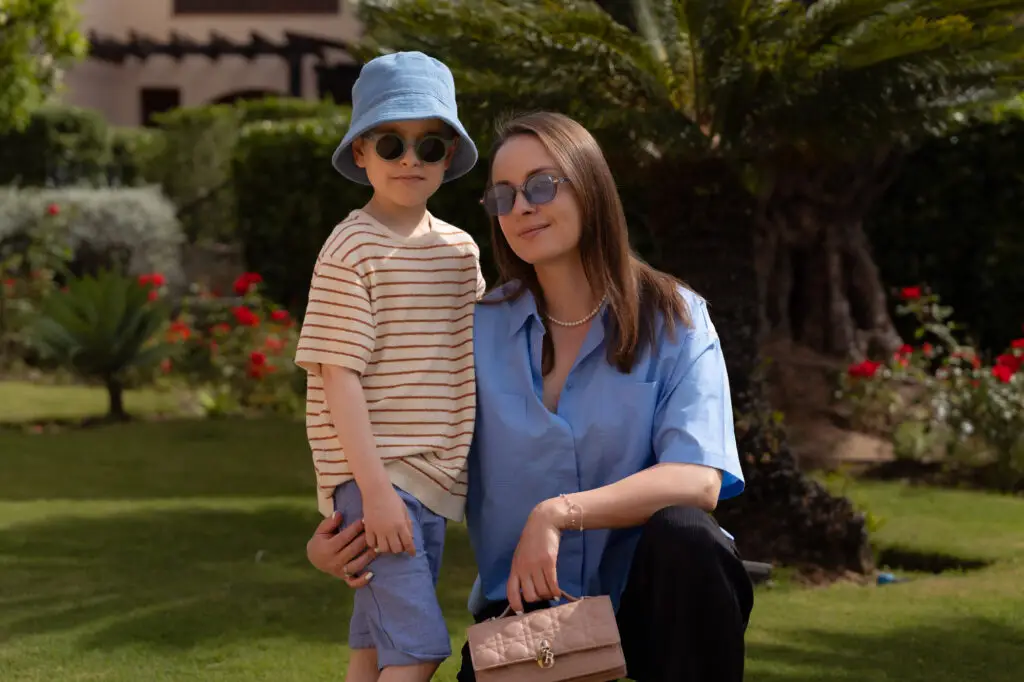 Mother and son wearing sunglasses posing together in a sunny garden during a family vacation.