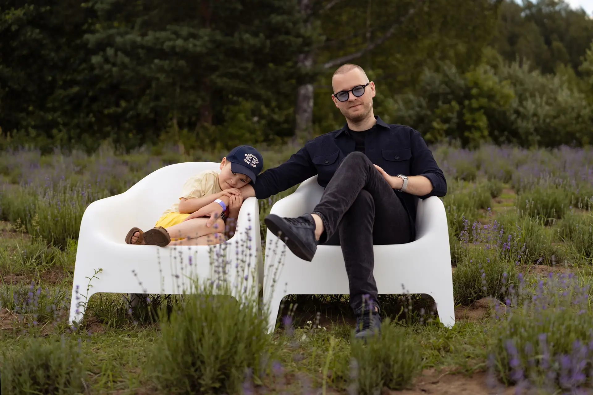 Father and son sitting on white chairs in a lavender field during a summer family vacation, sharing a calm and tender moment.