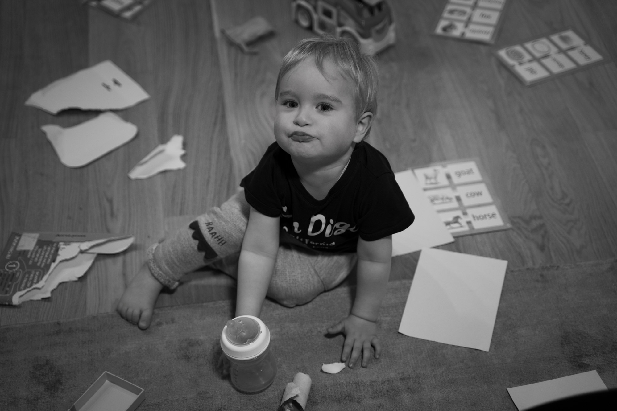 Little boy sitting on the floor with toys and papers around, candid indoor family photography in natural light.