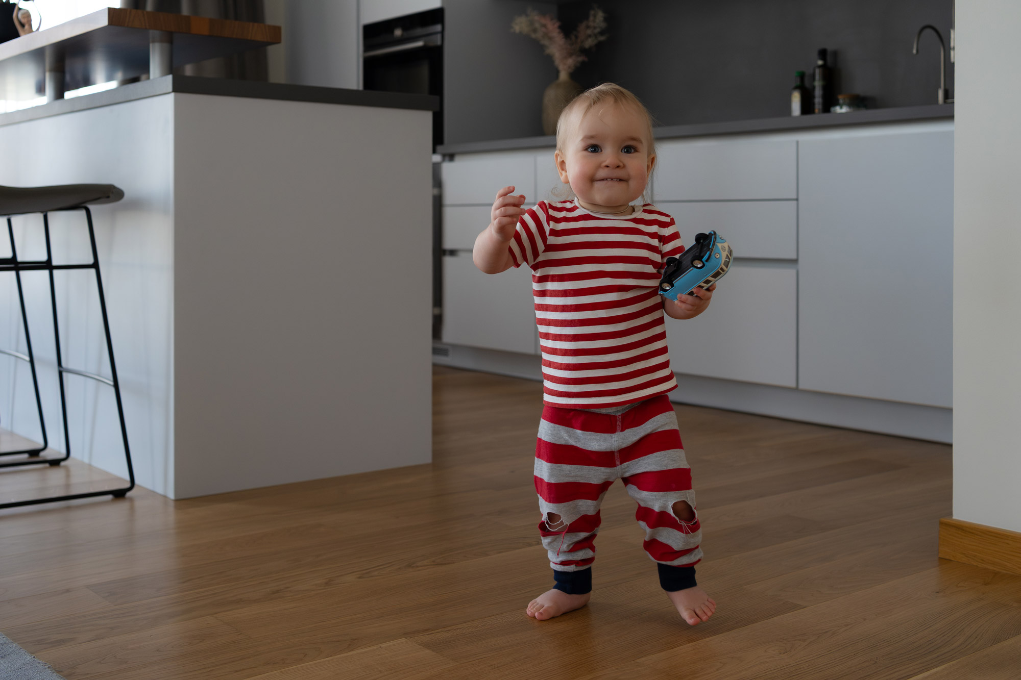 Little boy walking indoors with a toy car, candid family photography using fast shutter speed to freeze motion.