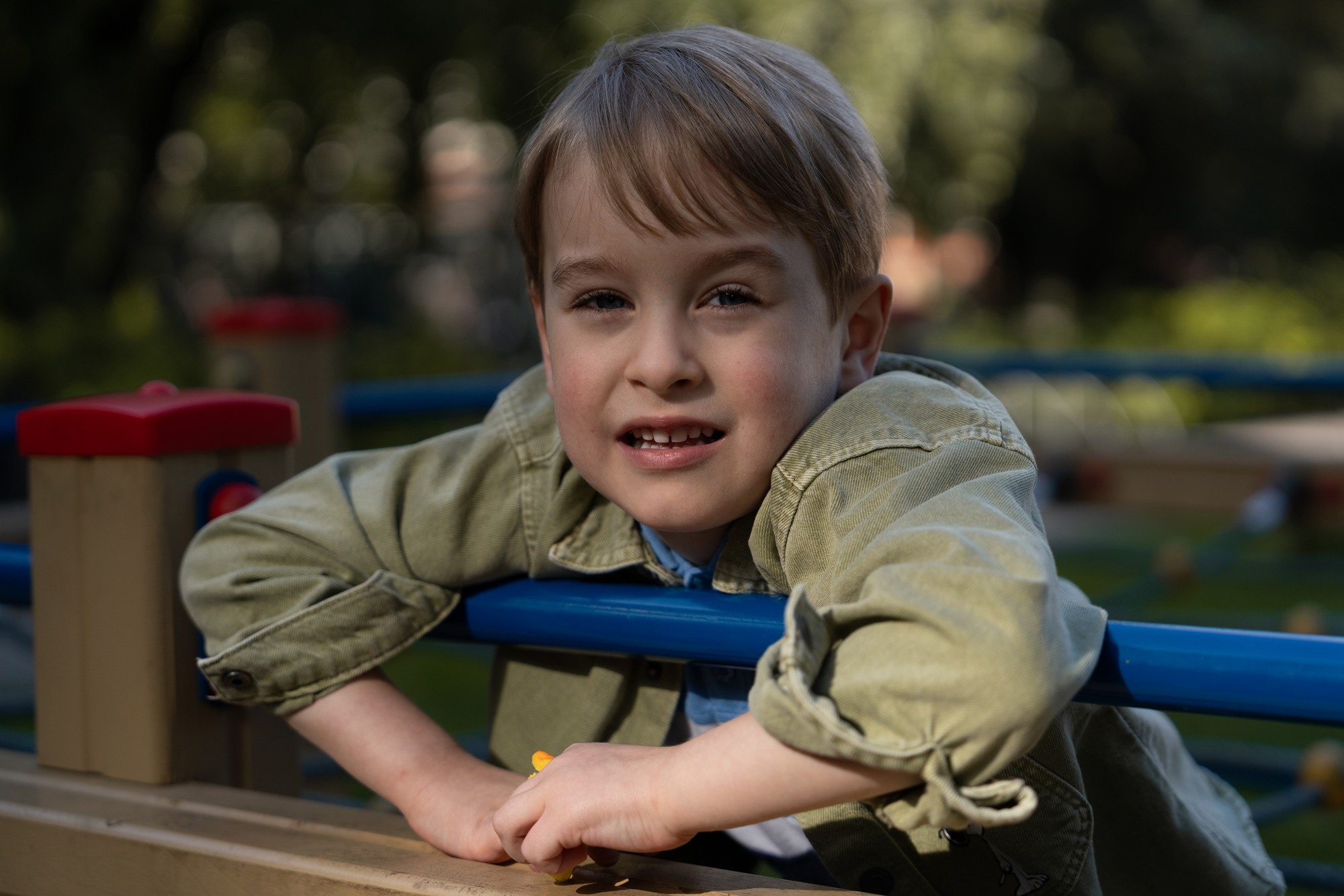 Portrait of a young boy smiling at a playground, leaning on a blue railing