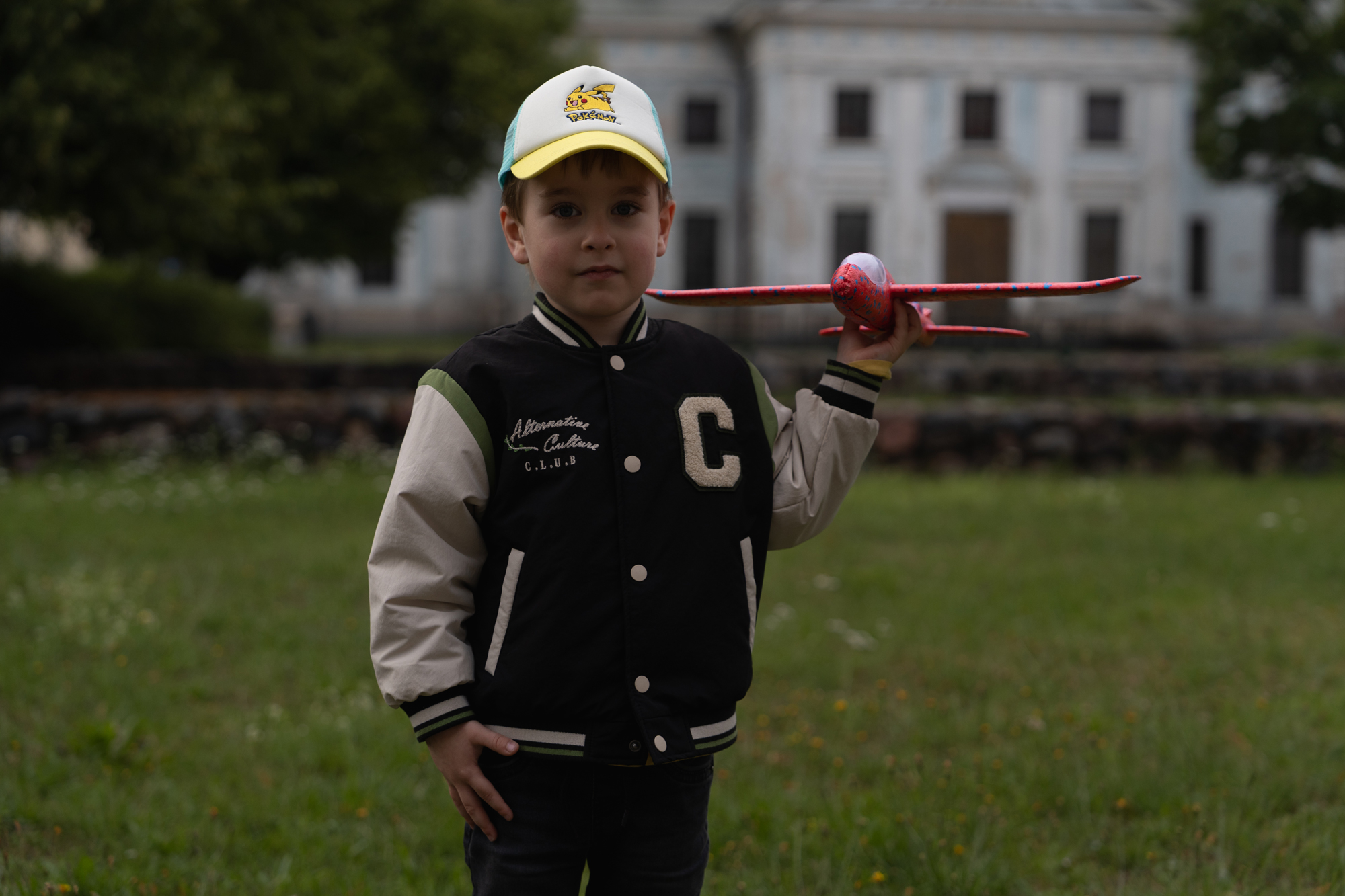 Original underexposed outdoor portrait of a young boy in a Pikachu cap holding a red toy airplane