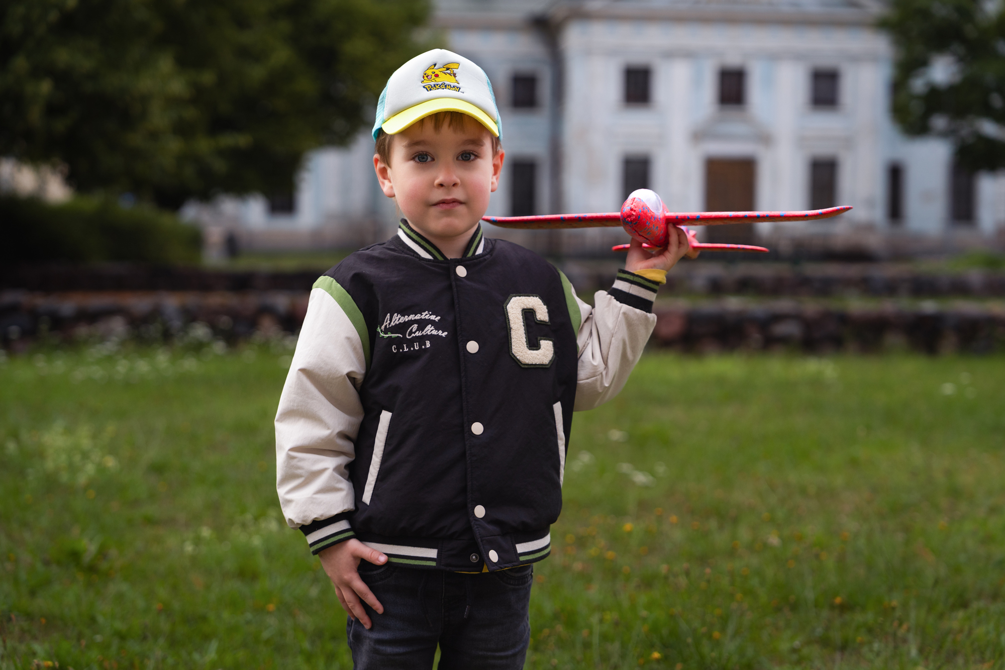 Edited outdoor portrait of a young boy in a Pikachu cap holding a red toy airplane with bright colors and balanced lighting