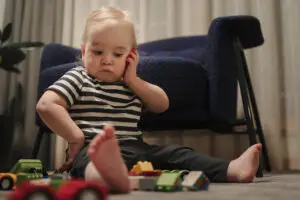 Toddler sitting on the floor playing with toy cars and blocks, captured in a candid low-angle family storytelling photo.