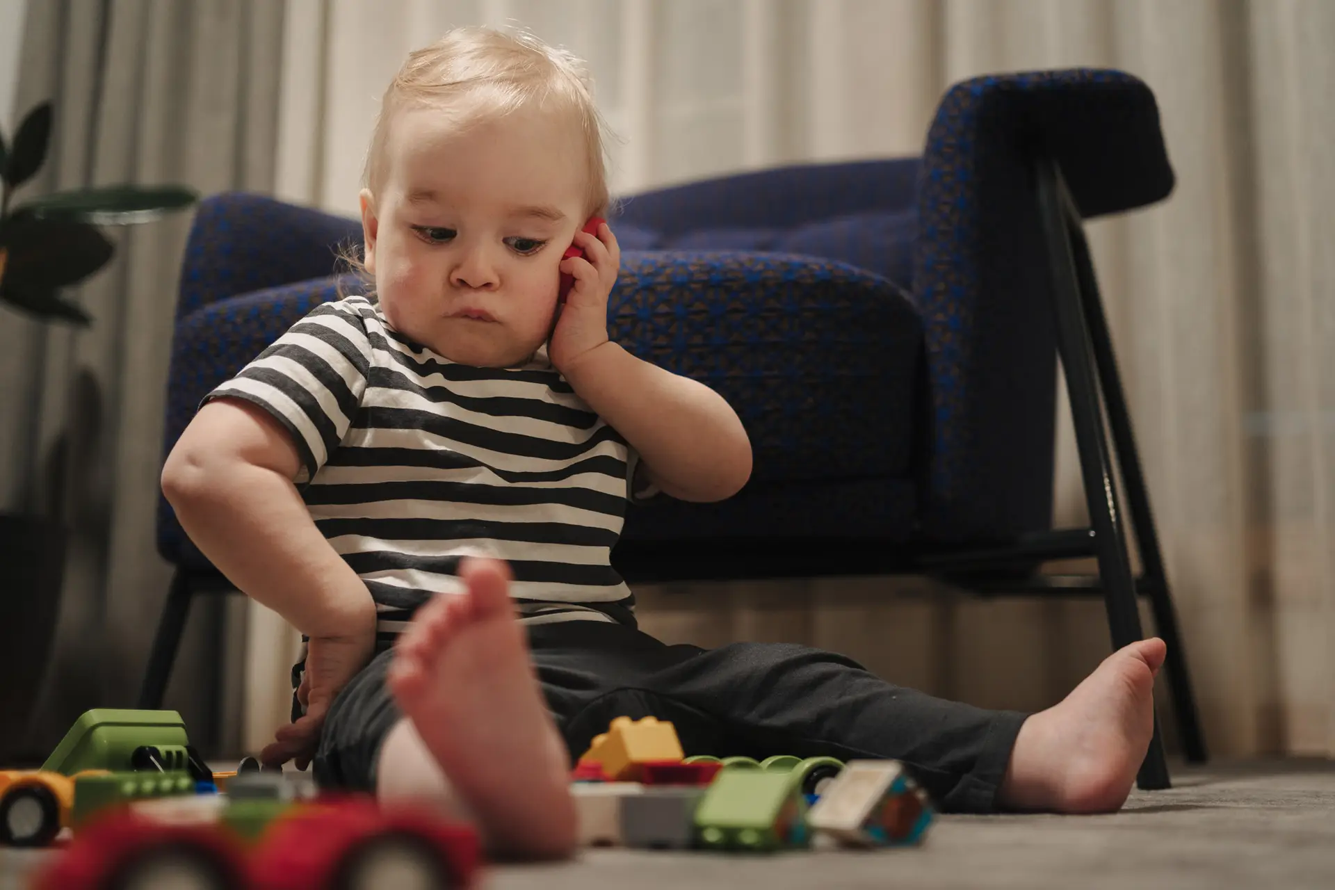 Toddler sitting on the floor playing with toy cars and blocks, captured in a candid low-angle family storytelling photo.